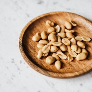 Top view of roasted peanuts in a wooden plate placed on a marble surface.